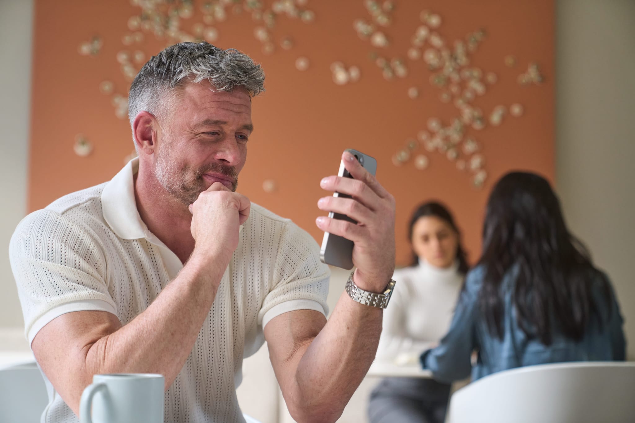 A man sitting at a table inside while looking at his phone. 