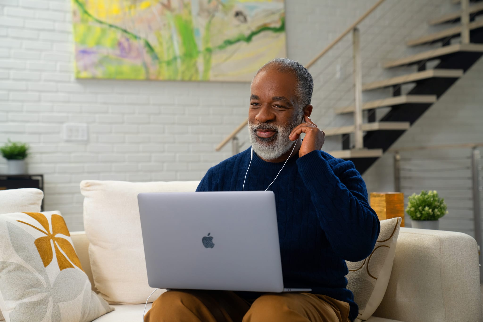 A man takes an online hearing test with headphones while sitting on a couch. 