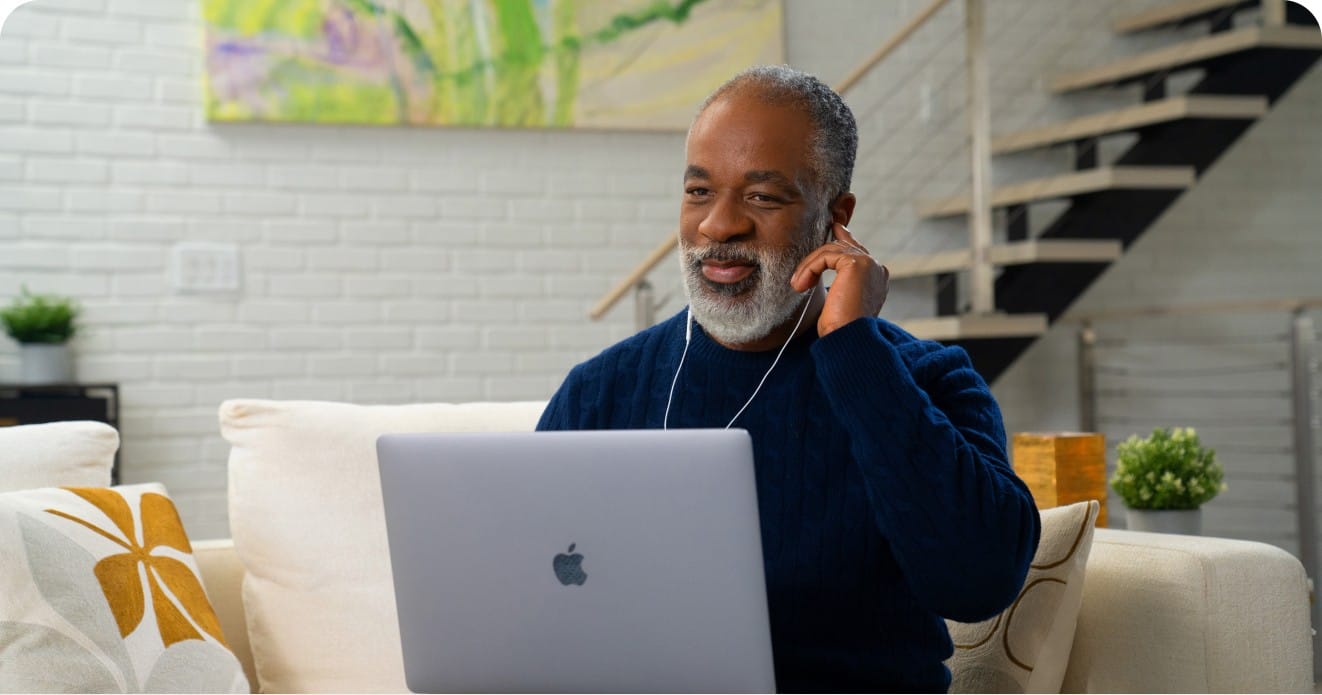 A man takes an online hearing test with headphones while sitting on a couch.